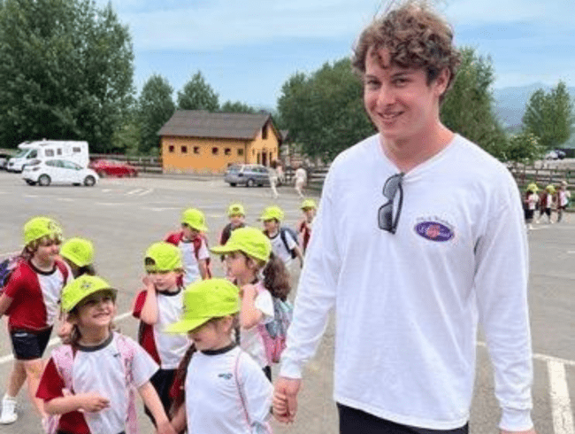 a young white man wearing a long sleeved white shirt with a group of kids