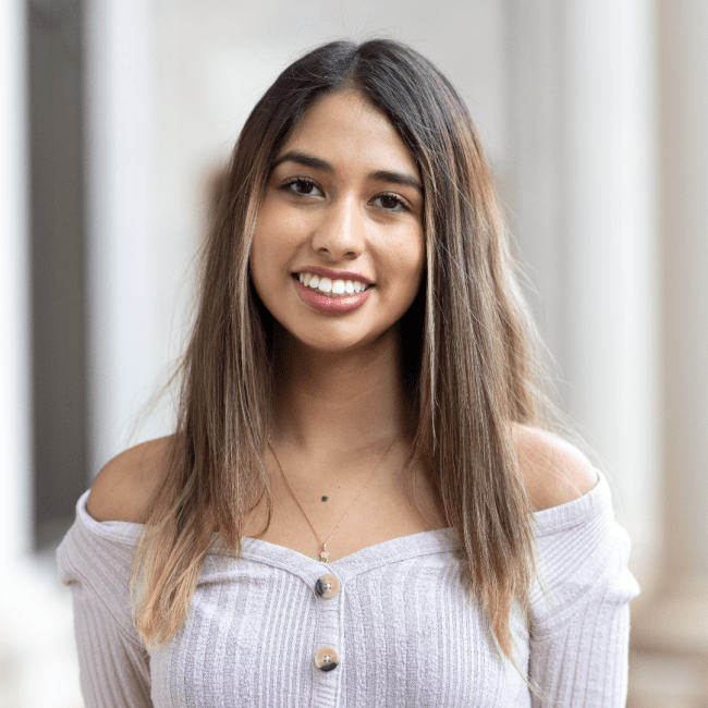 a young woman wearing a lavender top with brown hair smiles