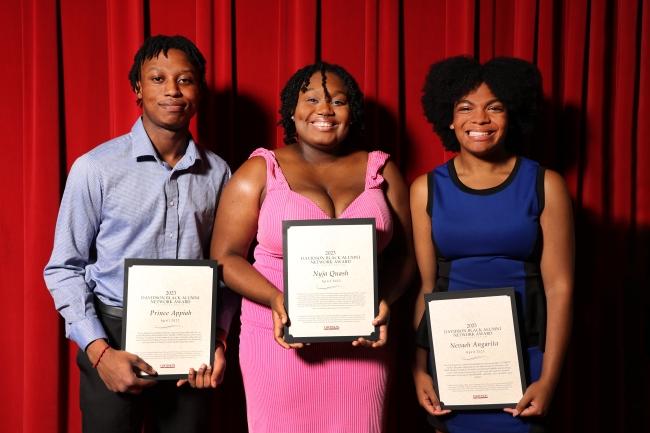 three young Black people holding awards against a red background