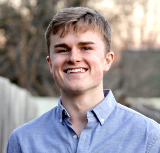 a young white man smiling wearing a blue collared shirt