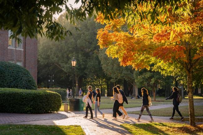 students walk on a brick pathway while fall foliage glows in the background