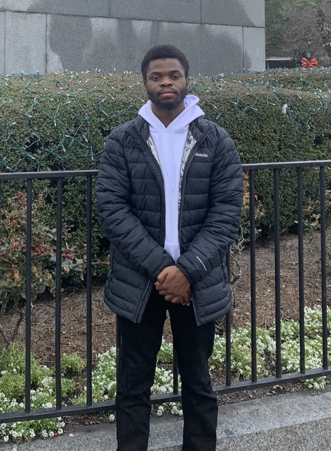 a young Black man wearing a white sweatshirt and black jacket