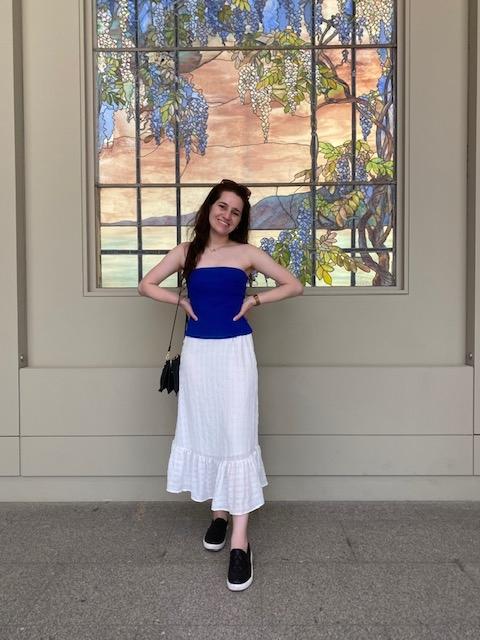 a young woman wearing a blue top and white skirt stands in front of a stained glass window