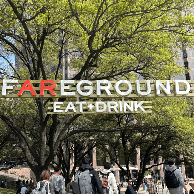 a green tree with a sign in front of it that reads "FAREGROUND EAT + DRINK"