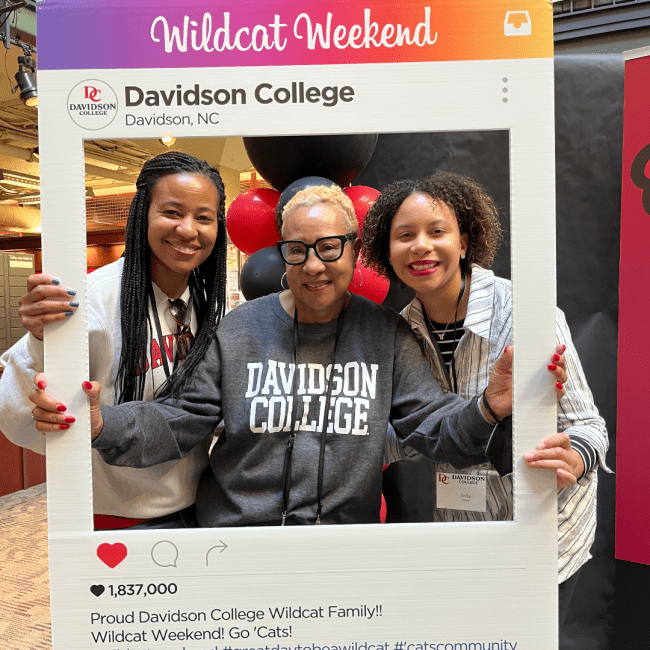 a family takes a picture together holding an Instagram cutout that reads "Wildcat Weekend"