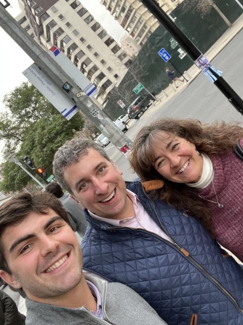 a young white man takes a selfie with an older man and woman on a city street