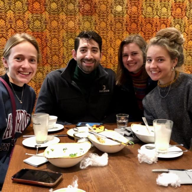 three young women and a young man smile while sitting around a restaurant table together