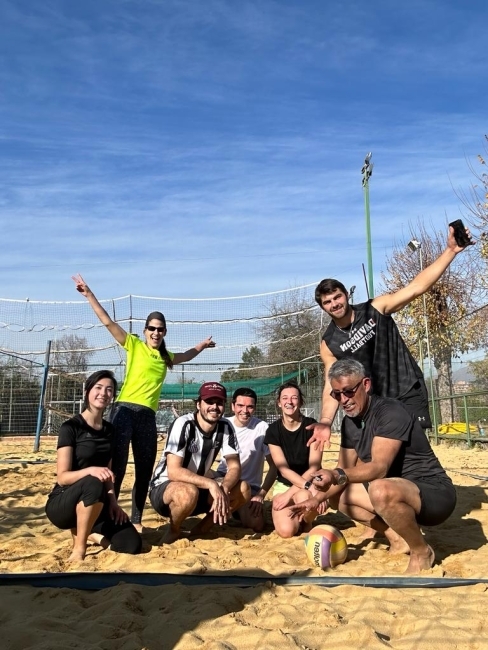 a group of young men and women squat in a sandy beach volleyball court