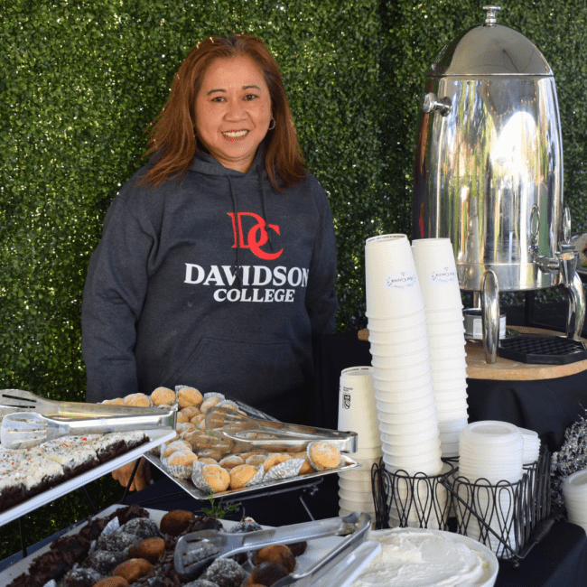 a young woman wearing a Davidson College sweatshirt stands behind a hot chocolate bar