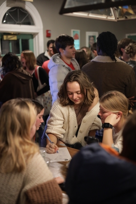 a group of four young women stand around a table working on a piece of paper