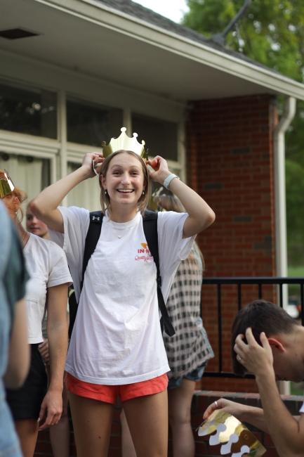 a young woman wears a tshirt and a gold crown while smiling outside