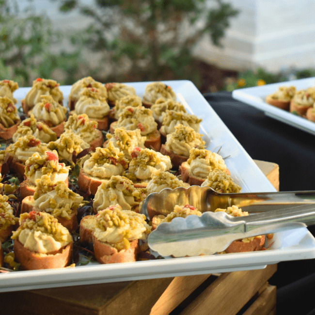 a stack of crostinis on a white plate with greenery in the background