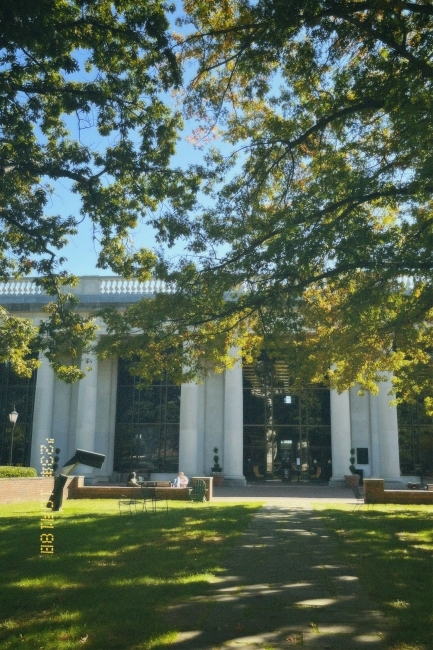 a green space filled with sculptures and trees in front of a building with columns