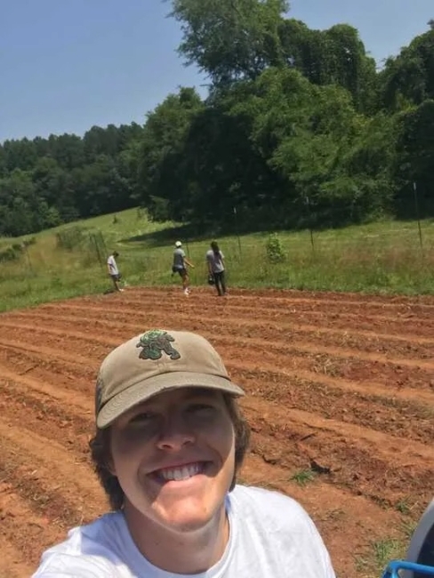 a young white male wearing a baseball cap with farmfields in the background