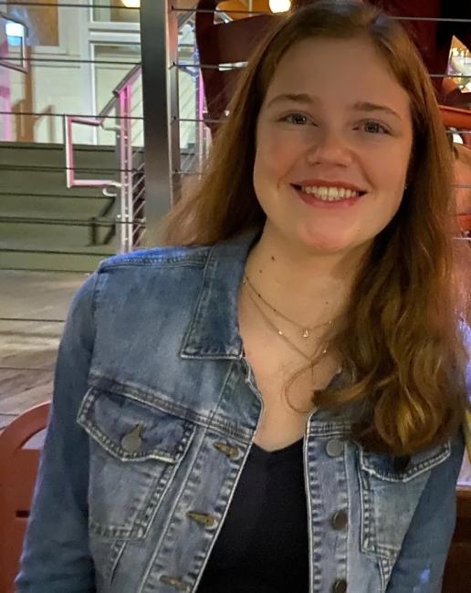 a young white woman with curly brown hair smiling and wearing a denim jacket