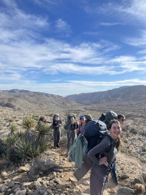 a group of young people hiking with backpacks and a desert in the background