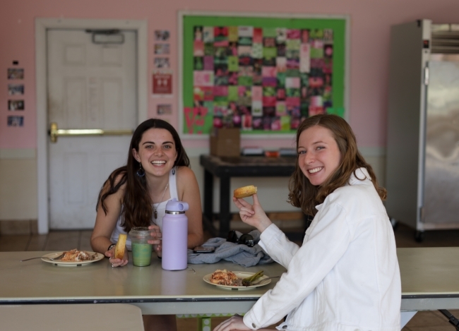 two young women sitting at a table together eating and laughing