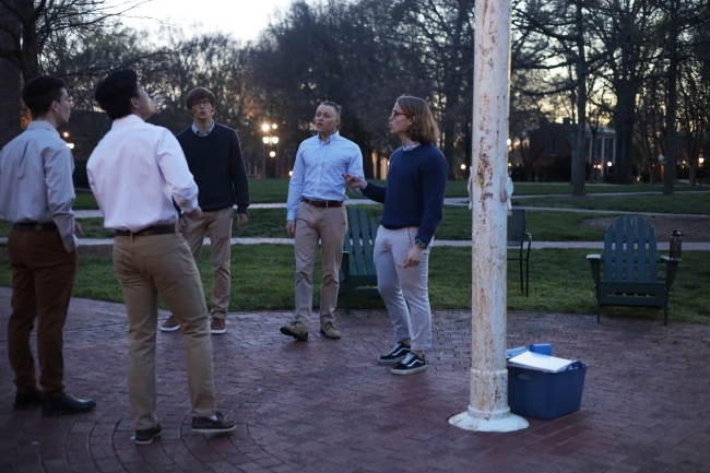 a group of young men wearing dress clothes standing outside at dusk