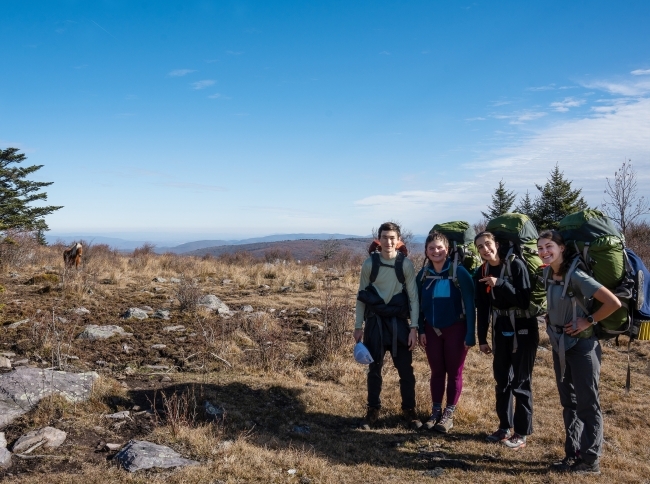 a group of four students wearing backpacks stand on a mountain top