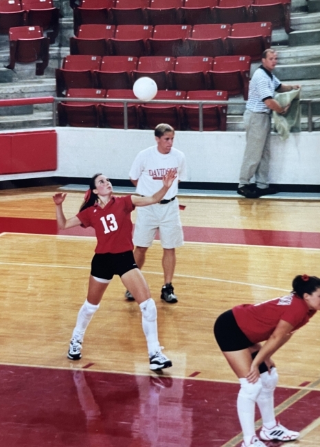 a woman wearing a Davidson uniform serving a volleyball