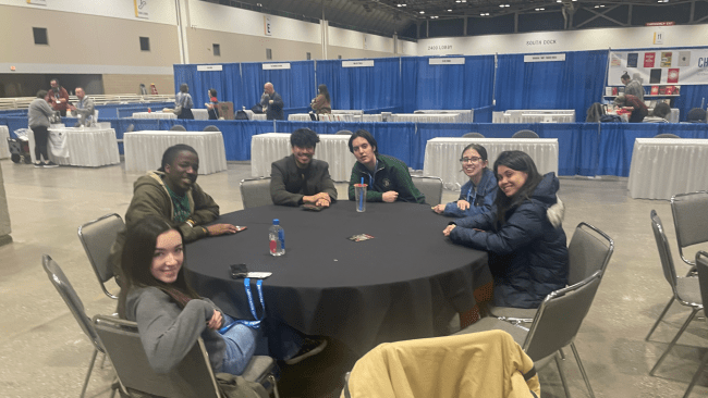 a group of young people sit around a table in a convention hall