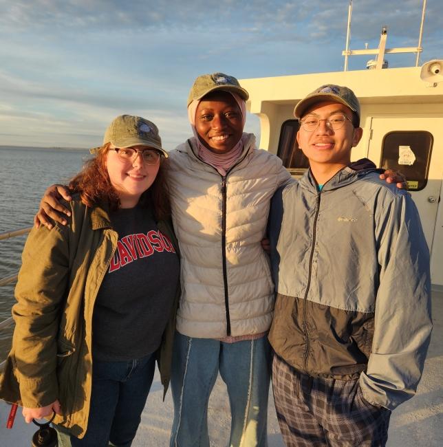 a group of three young people smiling together on a boat