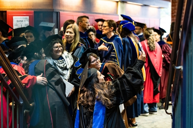 a group of people stand around in regalia while taking pictures and embracing