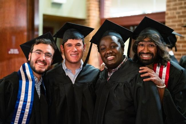 a group of young men in graduation regalia smile together