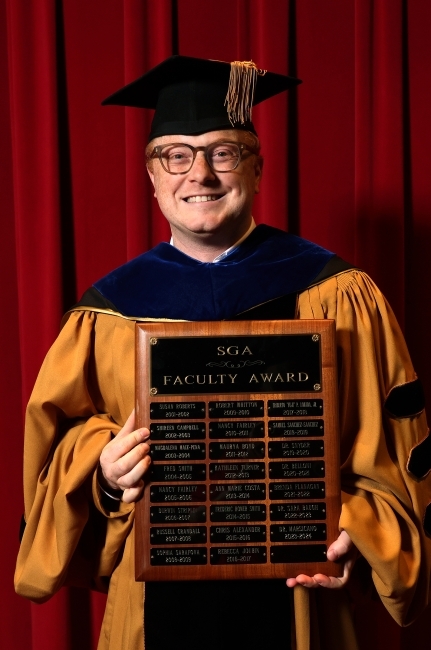 a young white man holding a wooden plaque