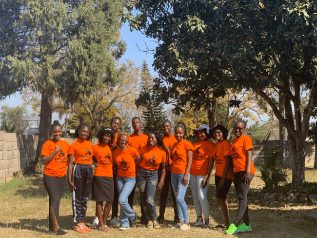 a group of young Black people in orange t-shirts stand together smiling
