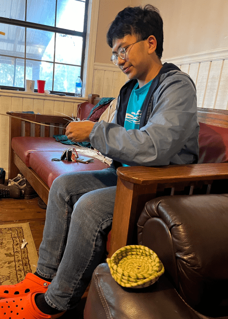 a young man holds straw while weaving a basket