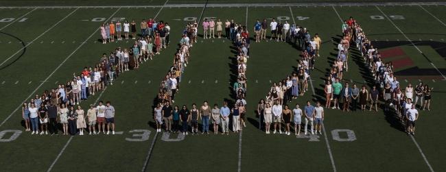 a group of students stand on a football field spelling out "2024"