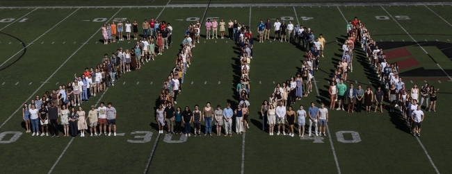 a group of students stand on a football field spelling out "2024"