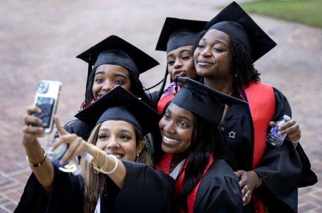 a group of young people in graduation caps and gowns smile while taking a selfie