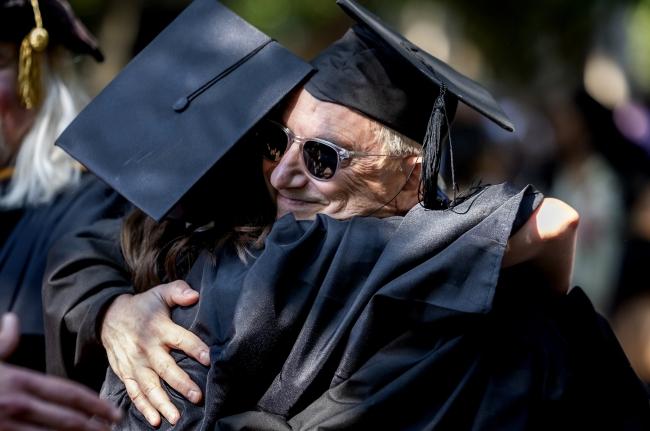 a young woman embraces an older man while in graduation robes