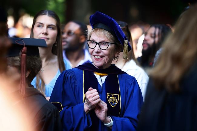 an older white woman in graduation robes smiles
