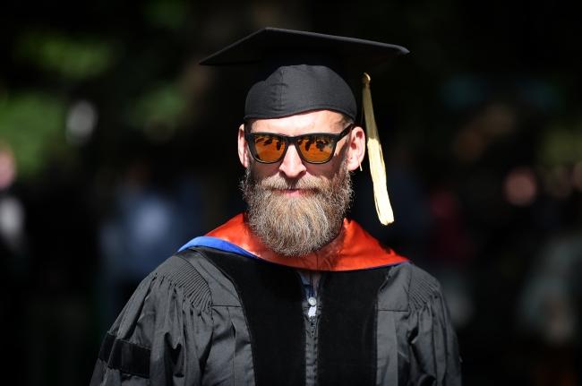 a faculty member wearing sunglasses and academic regalia smiles