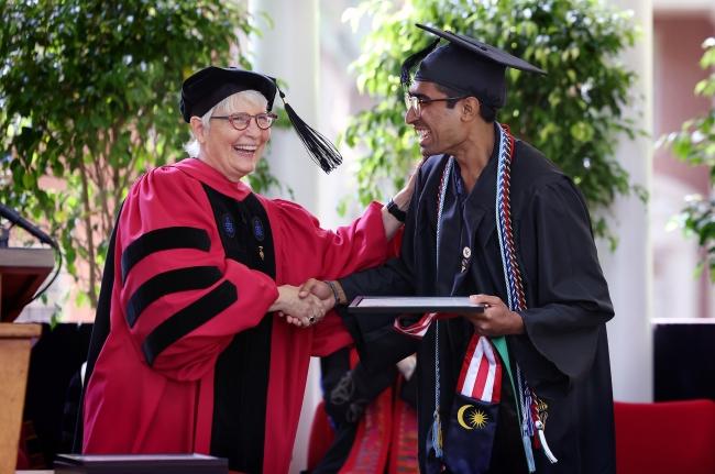 a young man accepts a diploma from an older white woman