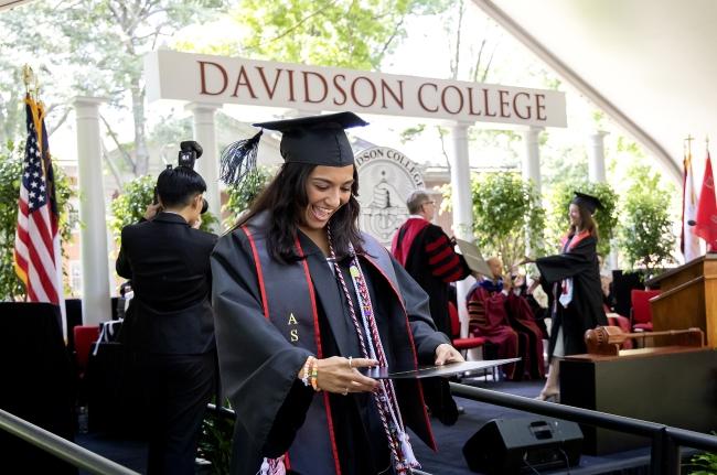 a young woman holds up her diploma looking at it 
