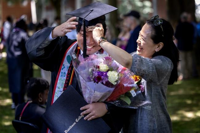 an Asian woman helps her son fix graduation cap while smiling