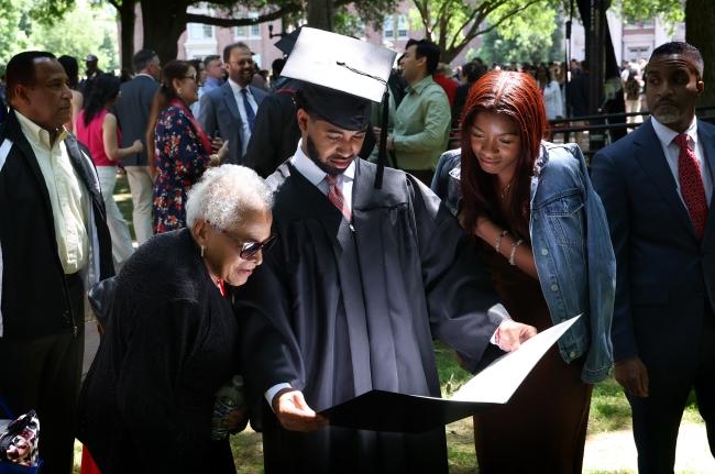 a young Black man shows his diploma to family while smiling