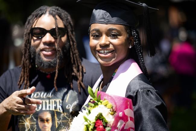 a young Black woman in graduation regalia smiles with her family