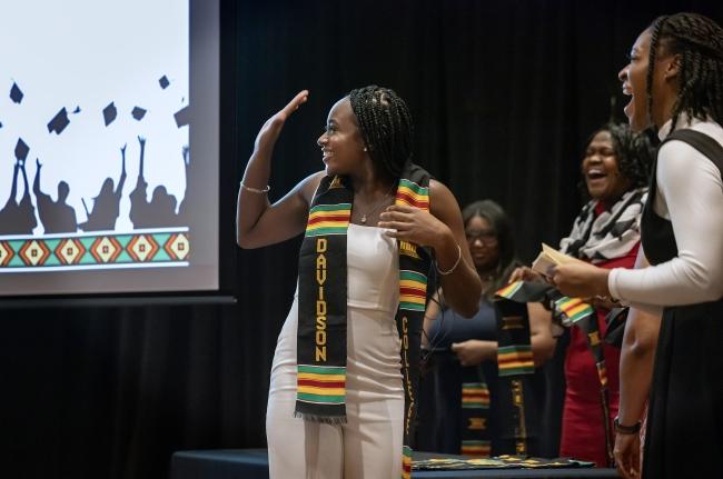 a young Black woman waves while accepting a stole