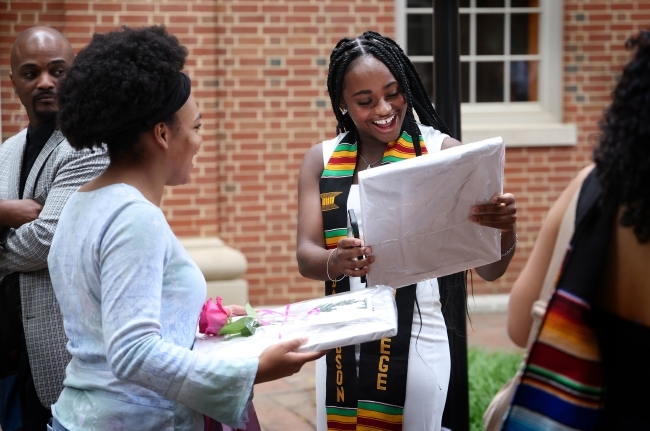 a young Black woman holds a diploma and smiles at it