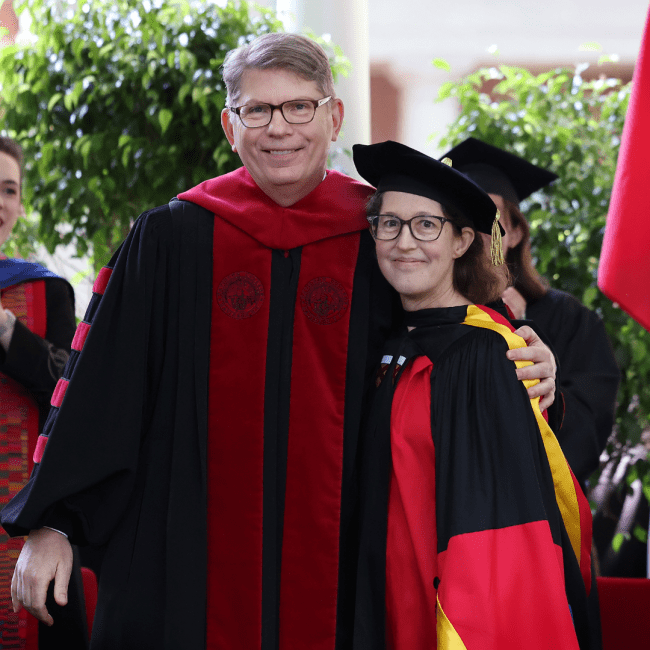 two adults in academic regalia embrace