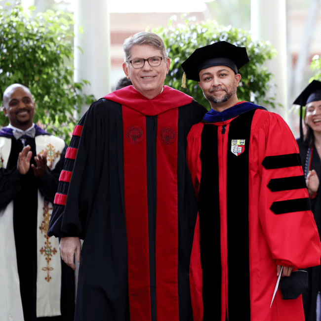 two adults in academic regalia embrace