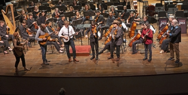 an Appalachian ensemble plays instruments while standing on a stage