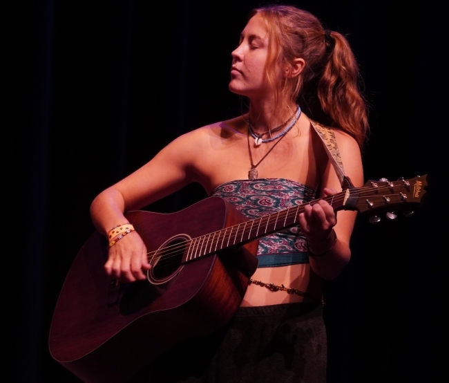 a young woman plays an acoustic guitar on a dark stage