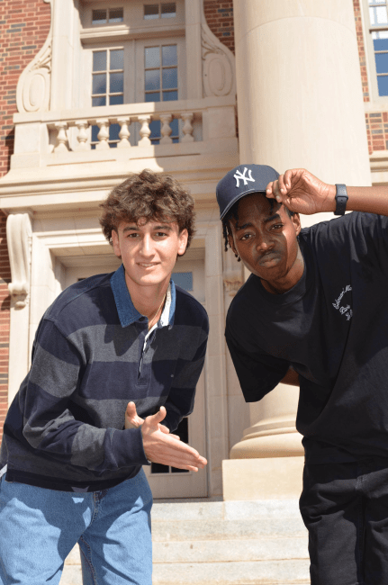 two young men standing together in front of a brick building