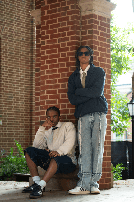 two young men stand in front of a brick wall